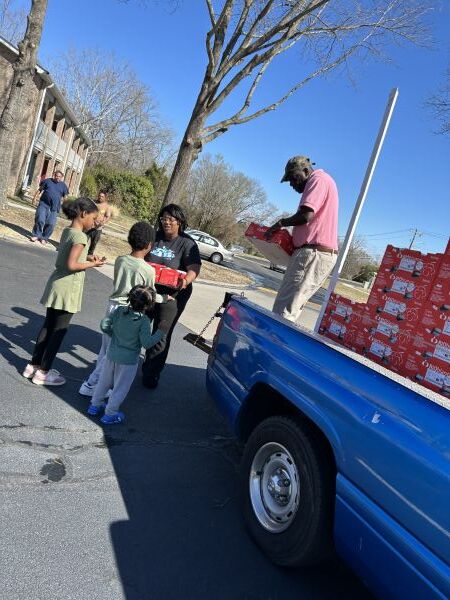 Individuals donating fresh fruit to children.