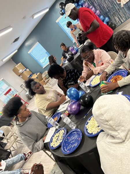 A group of teens sitting and eating around a table.