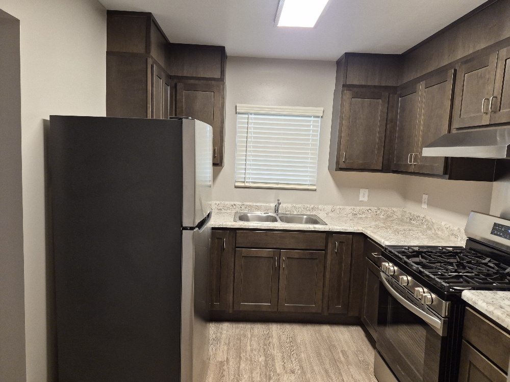A view of the kitchen, with the fridge on the left wall, sink straight ahead, and the stove on the right.
