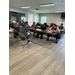  Multiple people sit at tables and listen to two people talk at the front of the room. 