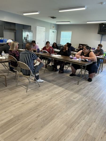 Budget1Small.jpg Multiple people sit at tables and listen to two people talk at the front of the room.