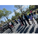  A group of people stand in a parking lot and listen to a woman speak. 