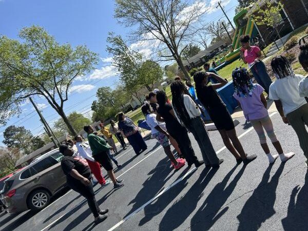 HW1Small.jpg A group of people stand in a parking lot and listen to a woman speak.