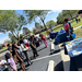  People stand in a parking lot by tables listening to a woman speak. 